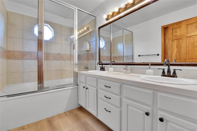 full bathroom with double vanity, wood finished floors, shower / bath combination with glass door, and a sink