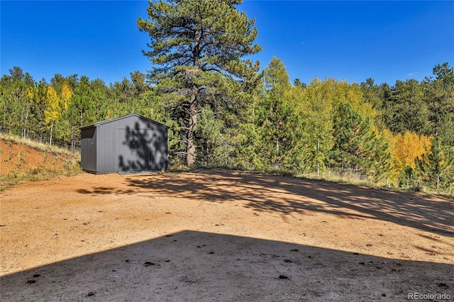 view of yard with an outbuilding, a wooded view, and a shed