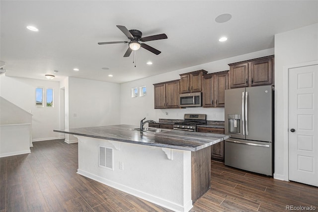 19096 E 55th Ave, Denver, CO 80249 - kitchen with stainless steel appliances, a sink, an island with sink, a ceiling fan, and dark countertops