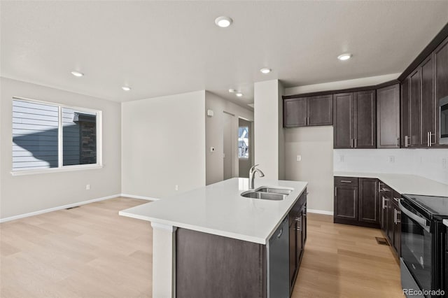 kitchen with range with electric stovetop, an island with sink, black dishwasher, sink, and light hardwood / wood-style flooring