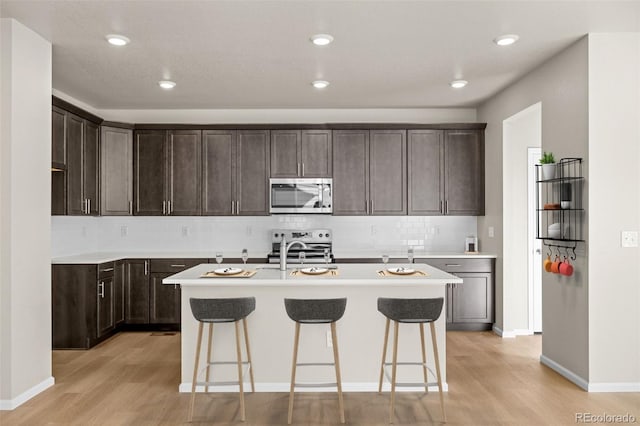 kitchen featuring a kitchen island with sink, backsplash, light wood-type flooring, and appliances with stainless steel finishes