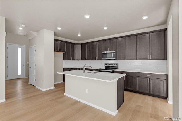 kitchen featuring sink, a kitchen island with sink, stainless steel appliances, dark brown cabinets, and light wood-type flooring