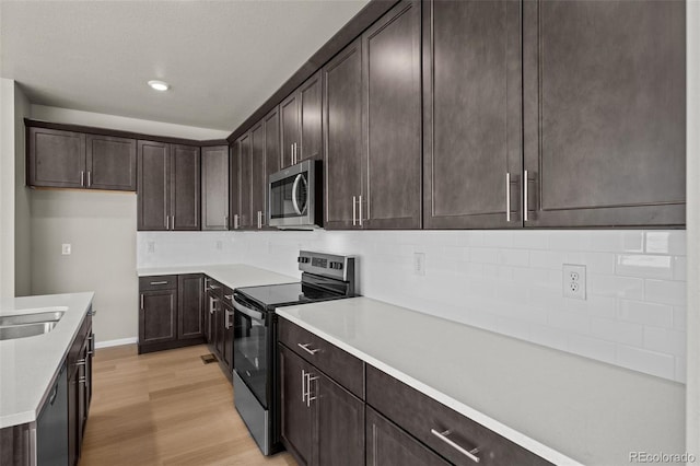 kitchen with stainless steel appliances, dark brown cabinets, backsplash, and light hardwood / wood-style floors