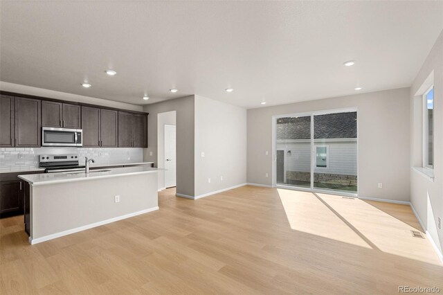 kitchen featuring dark brown cabinetry, a center island with sink, light hardwood / wood-style flooring, appliances with stainless steel finishes, and decorative backsplash