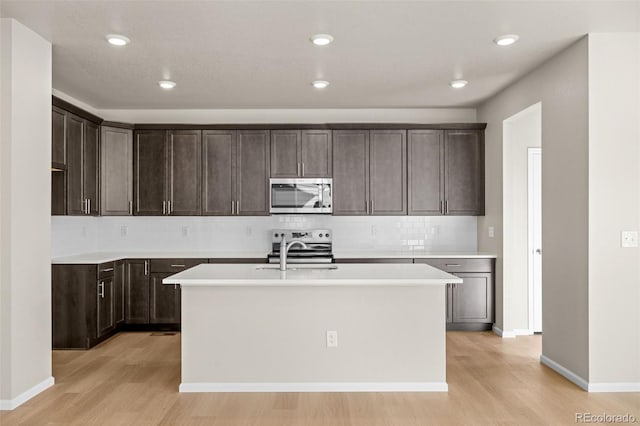 kitchen with stainless steel appliances, a kitchen island with sink, sink, and light wood-type flooring