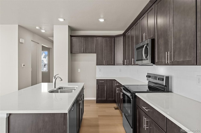 kitchen featuring sink, decorative backsplash, a kitchen island with sink, light hardwood / wood-style floors, and stainless steel appliances