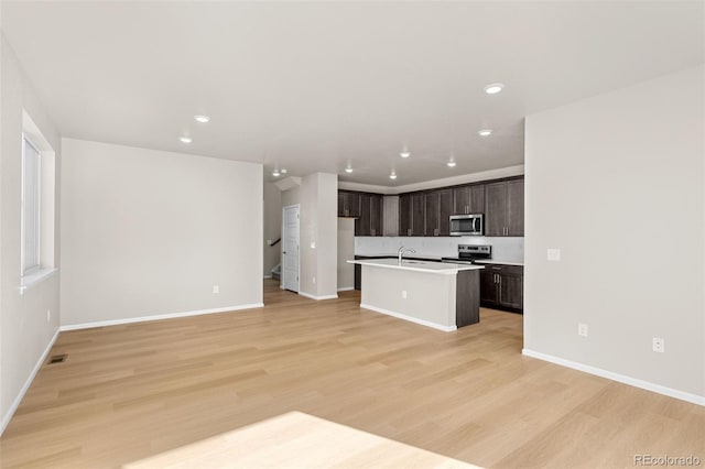 kitchen featuring sink, a kitchen island with sink, dark brown cabinets, stainless steel appliances, and light hardwood / wood-style floors