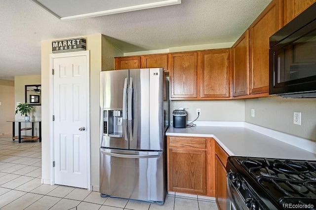 4863 Quail Ct, Frederick, CO 80504 - kitchen featuring stainless steel fridge, black microwave, light tile patterned floors, brown cabinetry, and a textured ceiling