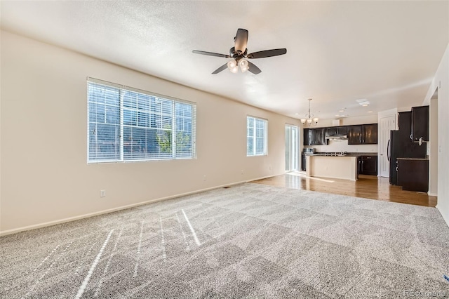 unfurnished living room with ceiling fan with notable chandelier, a textured ceiling, and carpet floors