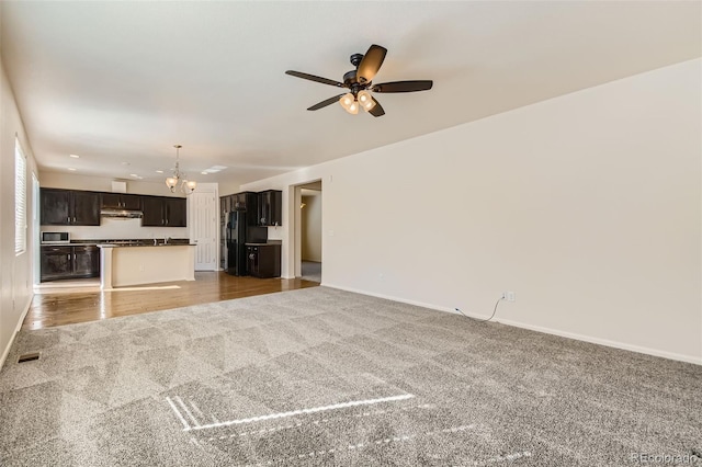 unfurnished living room with ceiling fan with notable chandelier, baseboards, and light colored carpet