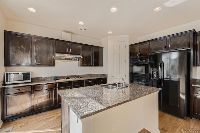 kitchen with light hardwood / wood-style floors, sink, black appliances, dark brown cabinets, and a center island with sink