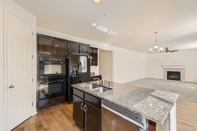 kitchen featuring a tiled fireplace, light hardwood / wood-style floors, sink, black appliances, and a center island with sink