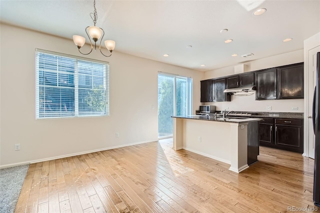 kitchen featuring light hardwood / wood-style floors, stone countertops, a chandelier, pendant lighting, and a center island with sink