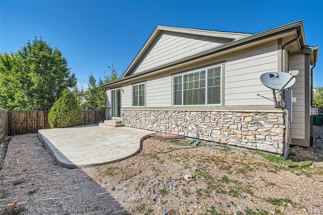 view of home's exterior featuring stone siding, a fenced backyard, and a patio