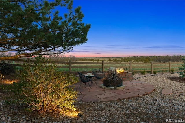 patio terrace at dusk with an outdoor fire pit, a rural view, and fence
