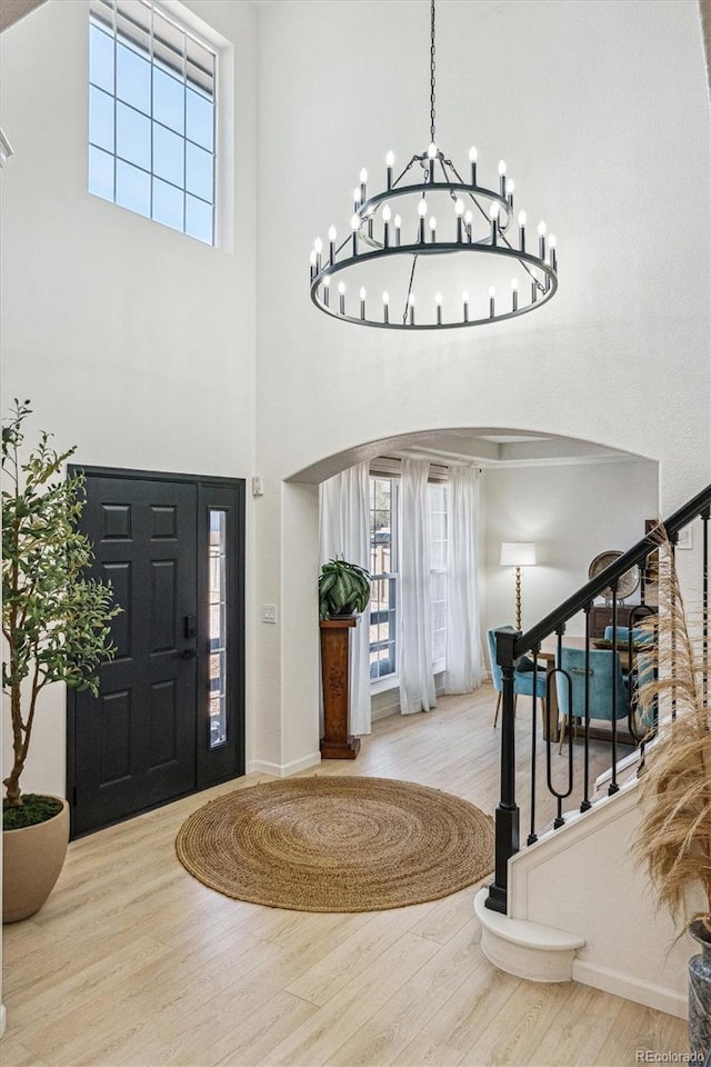 foyer with an inviting chandelier, wood finished floors, a high ceiling, a healthy amount of sunlight, and arched walkways