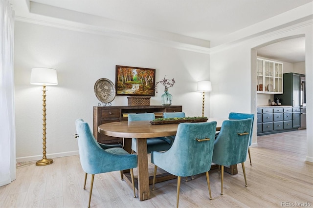 dining room featuring ornamental molding, baseboards, light wood-type flooring, and arched walkways