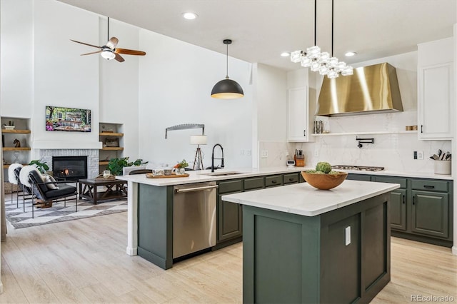 kitchen featuring a center island, a sink, stainless steel appliances, white cabinets, and wall chimney range hood