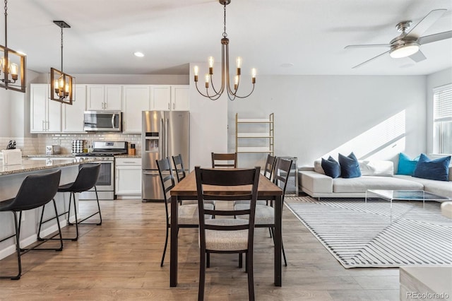 dining room with ceiling fan with notable chandelier and light hardwood / wood-style floors