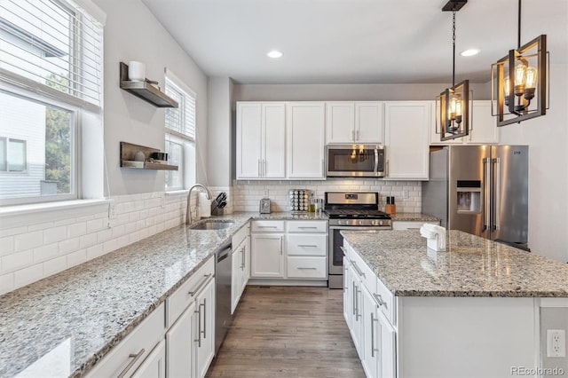 kitchen with pendant lighting, white cabinetry, sink, stainless steel appliances, and light stone countertops