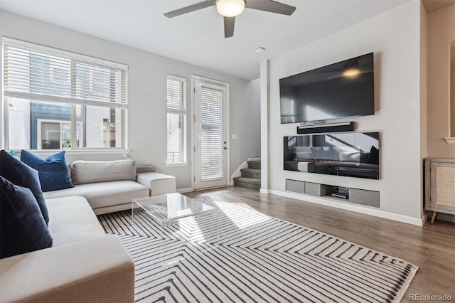 living room featuring a ceiling fan, baseboards, stairs, and wood finished floors