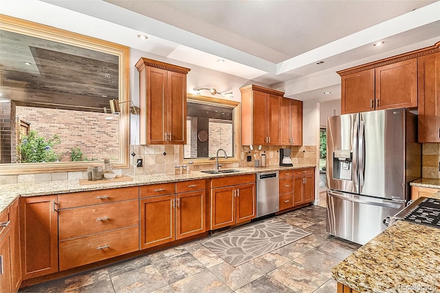 kitchen featuring light stone counters, sink, a tray ceiling, appliances with stainless steel finishes, and decorative backsplash