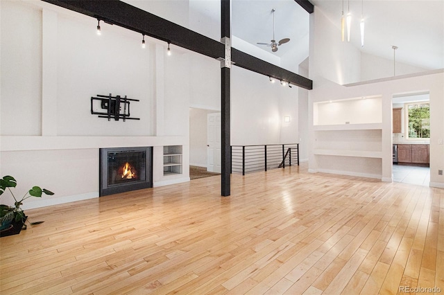 unfurnished living room featuring ceiling fan, built in features, light hardwood / wood-style flooring, high vaulted ceiling, and rail lighting