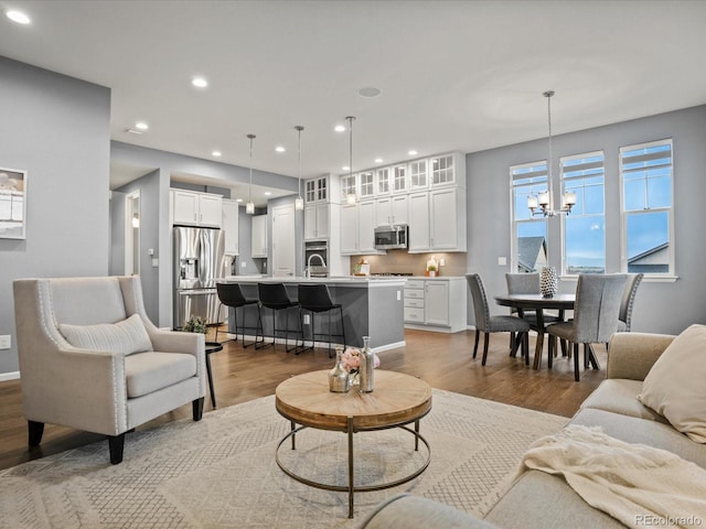 living area featuring a chandelier, light wood-style flooring, baseboards, and recessed lighting