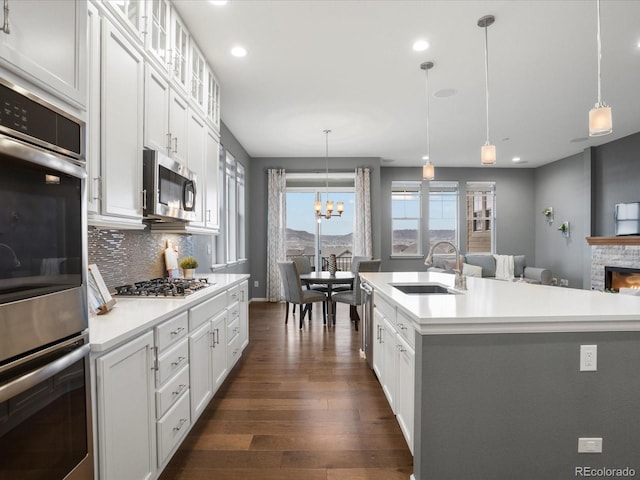 kitchen with a sink, stainless steel appliances, dark wood-style flooring, light countertops, and tasteful backsplash