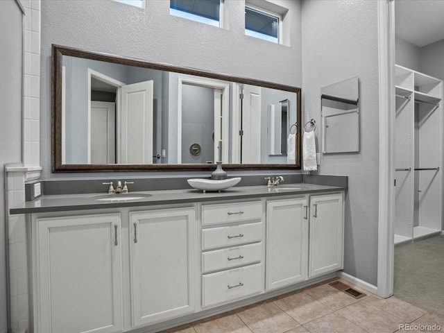 bathroom featuring a sink, double vanity, a textured wall, and tile patterned floors