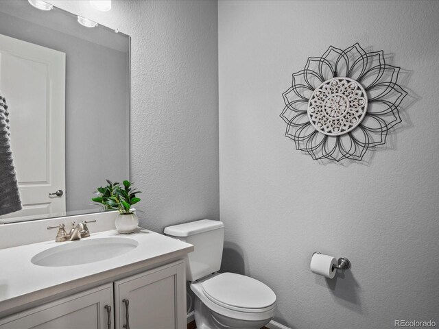 bathroom featuring toilet, vanity, and a textured wall