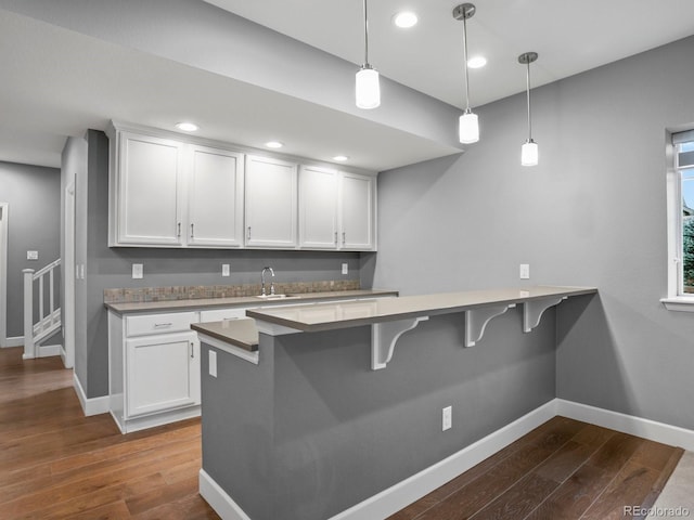 kitchen with a peninsula, dark wood-type flooring, baseboards, and a kitchen breakfast bar