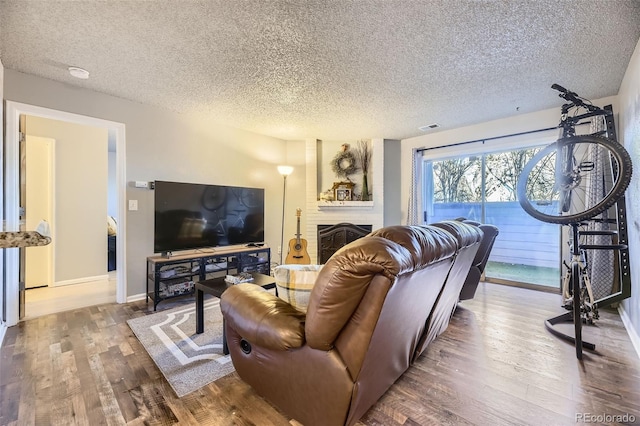 living room with a fireplace, visible vents, a textured ceiling, wood finished floors, and baseboards