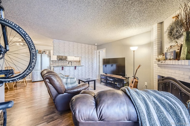 living area with a textured ceiling, a brick fireplace, and wood finished floors