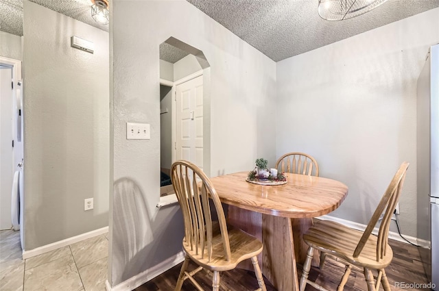 dining space featuring arched walkways, a textured wall, light tile patterned floors, a textured ceiling, and baseboards