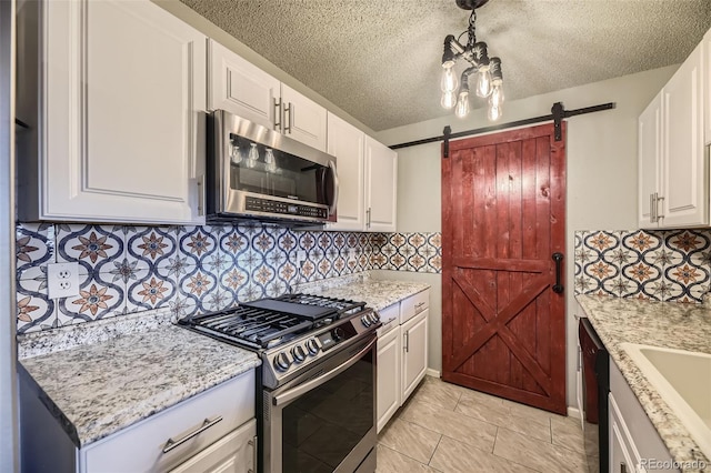 kitchen featuring backsplash, a barn door, appliances with stainless steel finishes, white cabinetry, and a sink