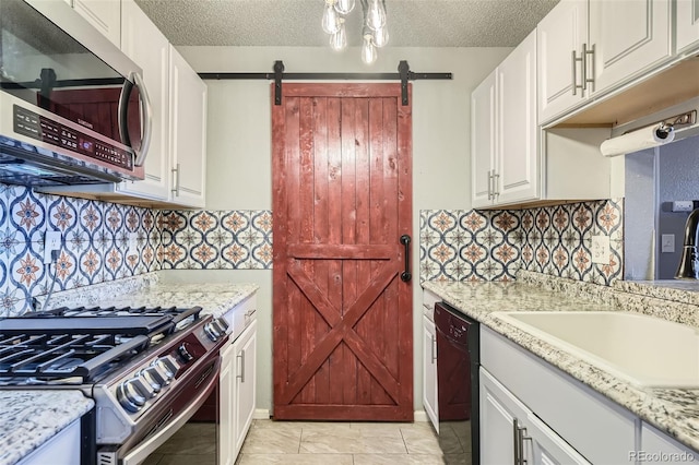 kitchen with white cabinets, light stone countertops, a barn door, and stainless steel appliances