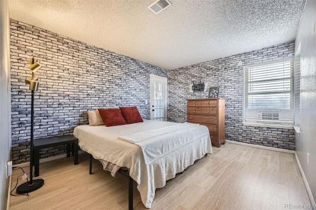 bedroom featuring light wood finished floors, brick wall, visible vents, and a textured ceiling