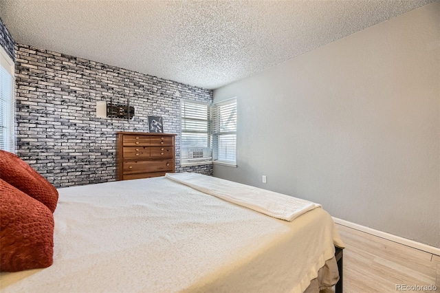 bedroom with a textured ceiling, brick wall, wood finished floors, and baseboards