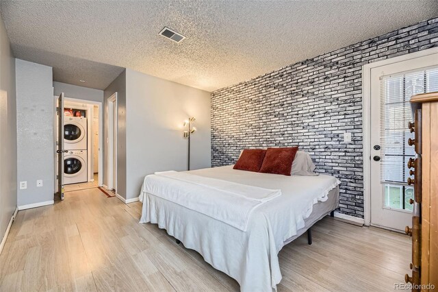 bedroom featuring stacked washer and dryer, light wood-type flooring, brick wall, and visible vents