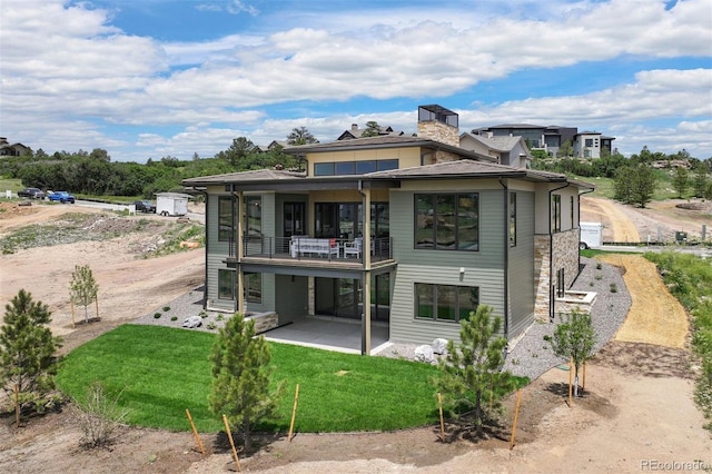 rear view of property featuring a yard, a balcony, and a patio