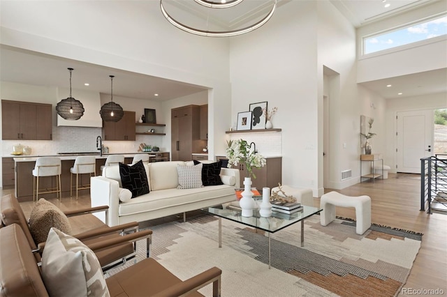 living room with sink, a high ceiling, and light hardwood / wood-style flooring