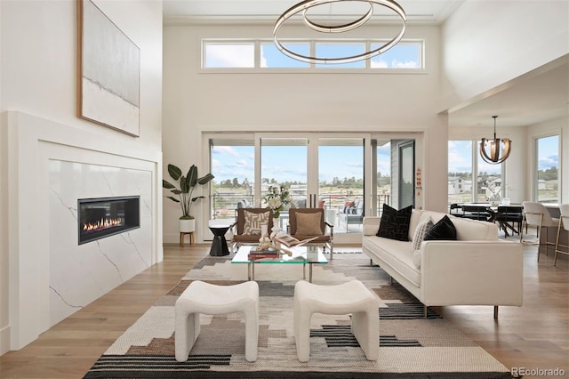 living room with a fireplace, light wood-type flooring, a towering ceiling, and a chandelier