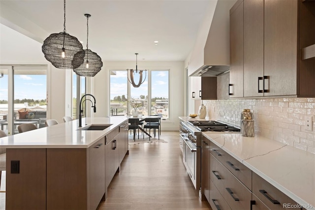 kitchen featuring sink, wall chimney exhaust hood, a notable chandelier, high end stainless steel range, and a center island with sink