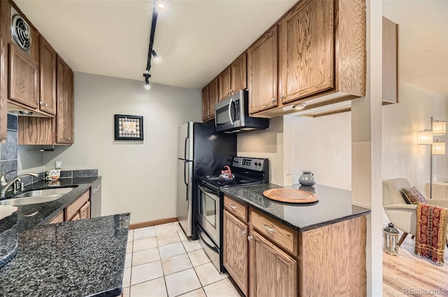 kitchen with stainless steel appliances, light tile patterned floors, rail lighting, dark stone counters, and sink