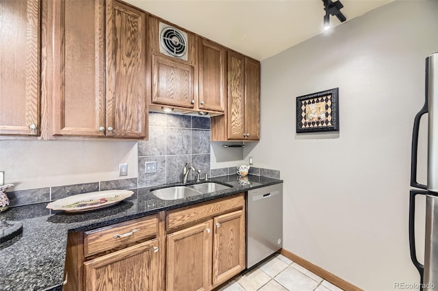 kitchen with stainless steel appliances, dark stone countertops, light tile patterned floors, and sink