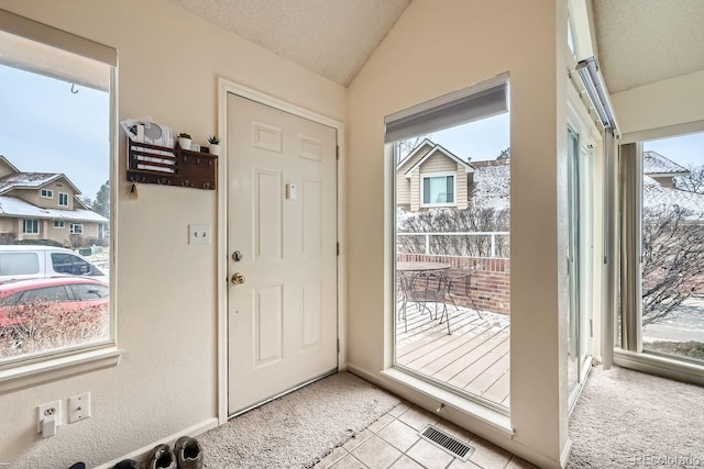 doorway with lofted ceiling, a textured ceiling, light tile patterned flooring, light colored carpet, and visible vents