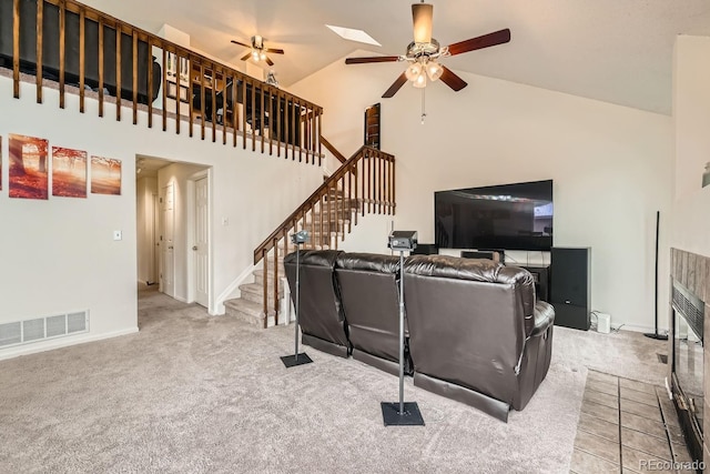 living area featuring carpet floors, visible vents, a ceiling fan, high vaulted ceiling, and stairs