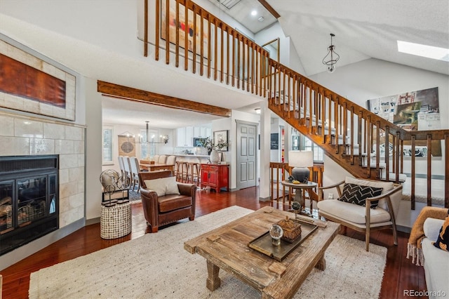 living room featuring lofted ceiling, a tiled fireplace, dark hardwood / wood-style floors, and a chandelier