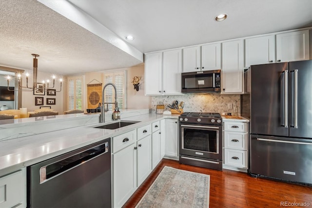 kitchen featuring kitchen peninsula, appliances with stainless steel finishes, a notable chandelier, white cabinets, and sink